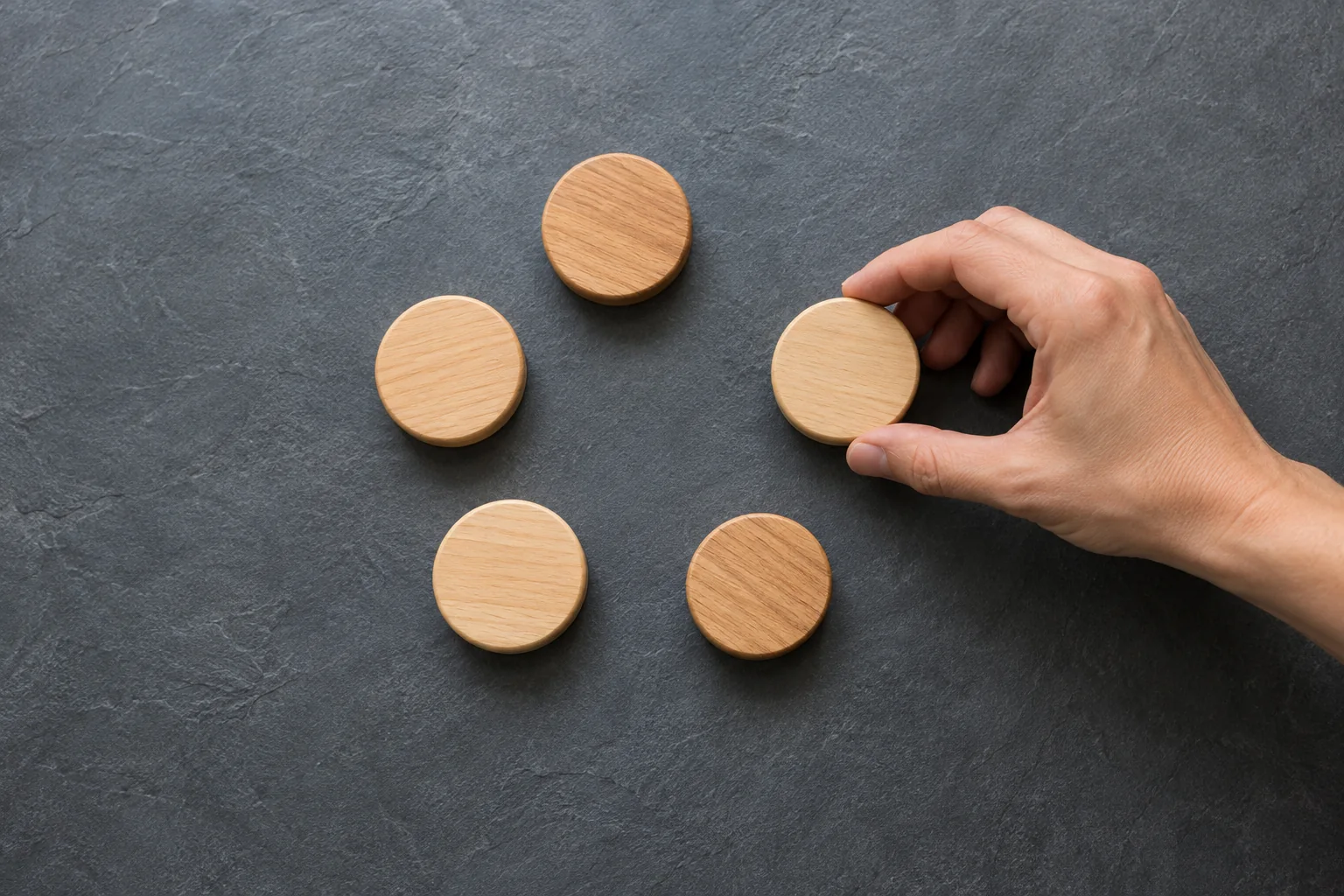 Mano ordenando cinco fichas de madera en un círculo incompleto
