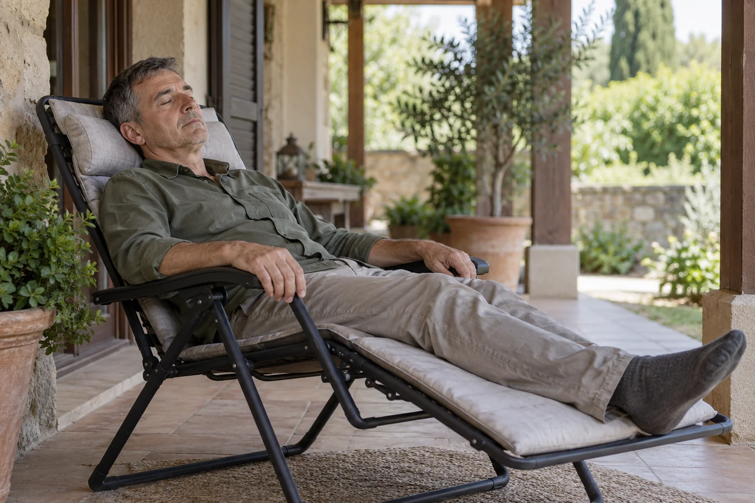 Un hombre descansa con los ojos cerrados en un sillón reclinable bajo un porche sombreado